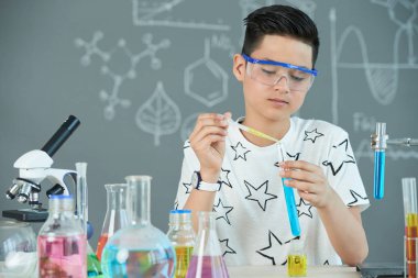 genç öğrenci çocuk giyen Emanet dökülen sarı sıvı test tüpüne gözlükler. 