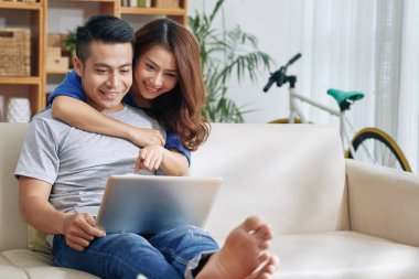 Güzel Asyalı Genç çift evde kanepede sörf dizüstü birlikte ve gülümseyerek