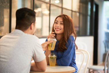 Arkadan görünüşü ile şirin Asyalı kadın ile soğuk içeceklerin paylaşımı ve gülerek kafeterya masada oturan adam 