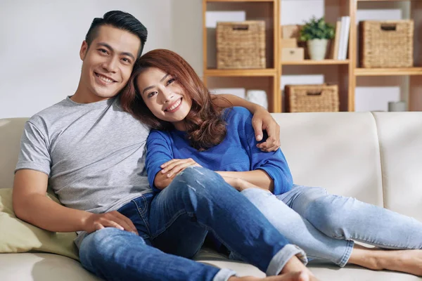 美丽的亚洲妇女和男子拥抱 而坐在沙发上 在家里和微笑的相机 — 图库照片