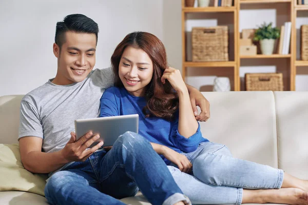 美丽的亚洲年轻夫妇拥抱和冷在家里的沙发上 而看平板电脑一起 — 图库照片