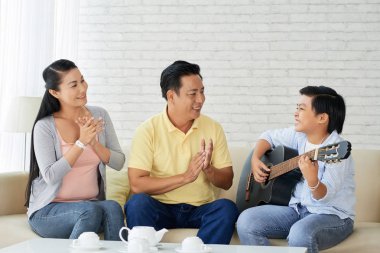 kanepede oturan ve alkış ebeveynler için gitar çalmak çocuk 