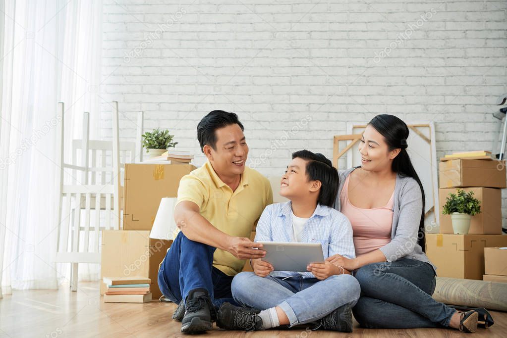 Asian mom, dad and son sitting on floor with digital tablet 