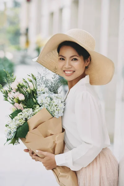 戴着夏日花束的草帽的迷人微笑的年轻女子 — 图库照片