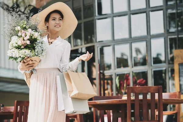 ペーパー バッグと屋外カフェに立って花を持つ魅力的な女性 — ストック写真