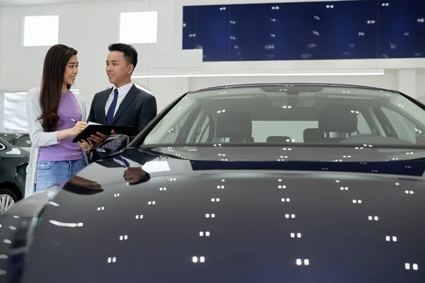 Sales man showing young woman where to sign document for new car