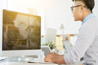 Masada oturan ve ofiste bilgisayar üzerinde çalışan genç Yöneticisi