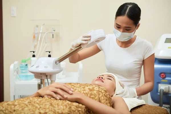 Kosmetolog Bär Gummihandskar Och Medicinska Ansikte Mask Stående Vid Behandlingsbord — Stockfoto