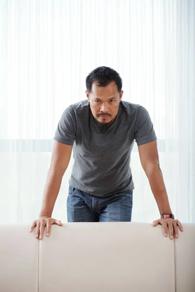 Angry Asian man leaning on sofa and looking at camera