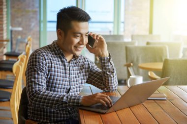 Dizüstü bilgisayarda çalışan ve telefonlara kafede Asya adam