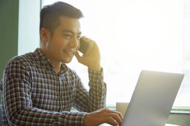 Café'de çalışma, cep telefonundan konuşuyor ve dizüstü bilgisayarda yazarak Asya genç Yöneticisi