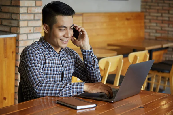 Lächelnder Mann Sitzt Café Und Telefoniert Und Tippt Auf Laptop — Stockfoto