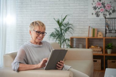 Gülümseyen yaşlı tablet bilgisayarda uygulama kullanan kadın