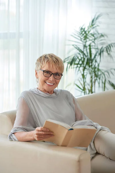 良い本と自宅で安静時笑顔のシニア女性 — ストック写真