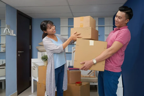 Asian couple packing carton boxes with household stuff and smiling happily while moving in new apartment