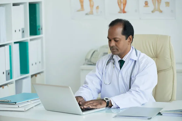 Seriöser Indischer Arzt Der Seinen Laptop Zur Arbeit Benutzt — Stockfoto
