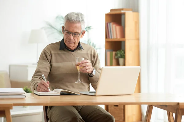 Starší Muž Pití Vína Při Práci Doma Tabulka Notebookem — Stock fotografie