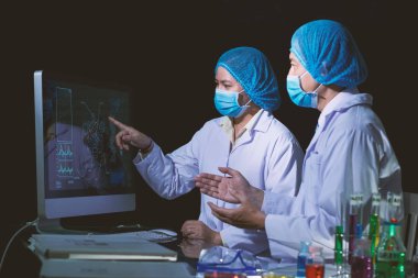 Araştırmacılar tıbbi maske ve istatistik verileri bilgisayar monitör laboratuvar eğitim beyaz ceket giyiyor