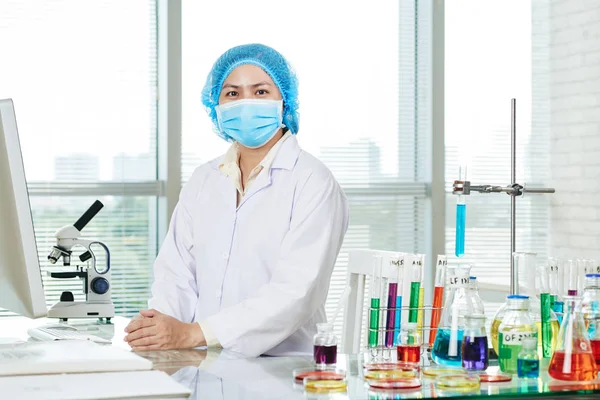 自信を持ってアジアの微生物研究室の机に白衣とマスクを着用 — ストック写真