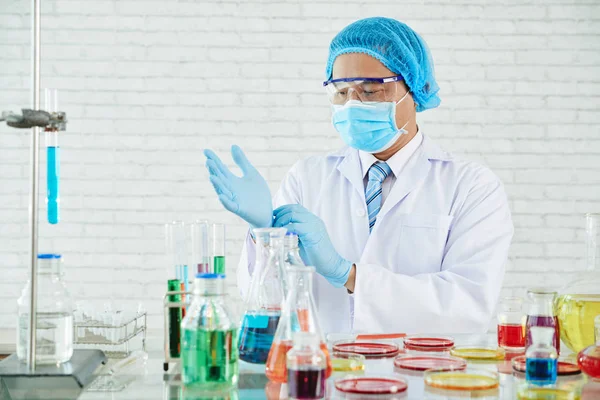 专业科学家穿着白大衣在实验室里用管子调节橡胶手套 — 图库照片