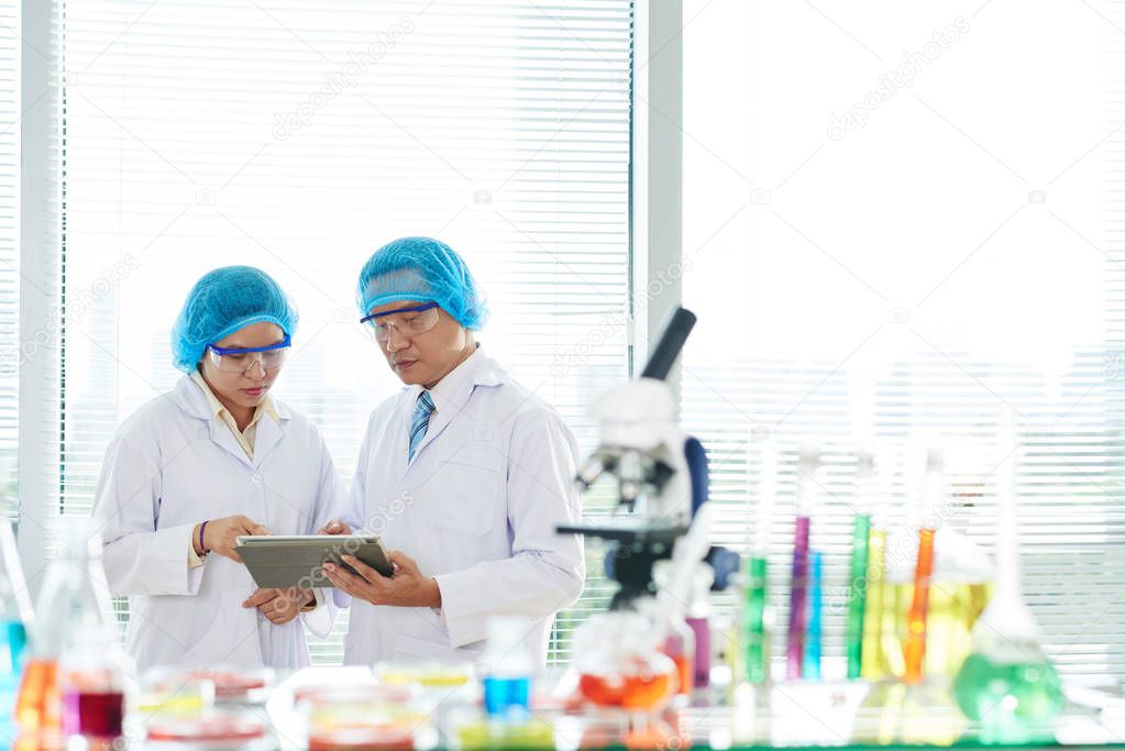 researchers working in laboratory with digital tablet and colorful tubes 