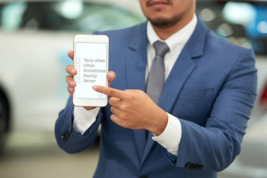 Anket soru için cevap seçenekleri ile akıllı telefon ekranını göstermeyi şık elbiseli otomobil satıcısı yakın çekim shot 
