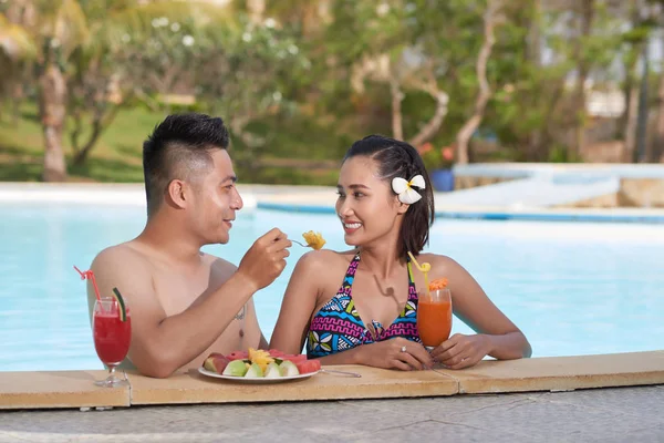 Beautiful Asian couple in love enjoying fresh fruits and cocktails in swimming pool