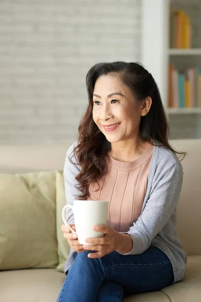 Happy elderly woman sitting with cup of coffee at home