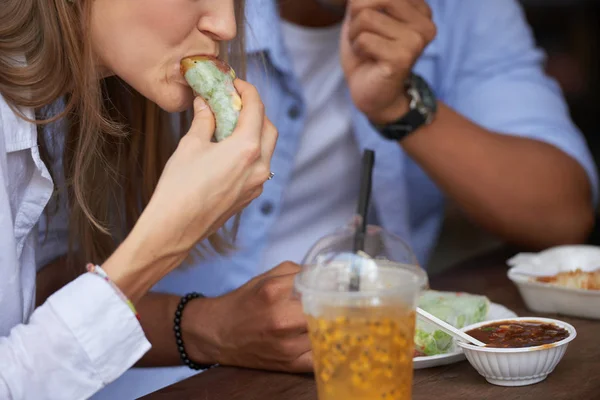 Young woman biting spring roll while having a lunch with her boyfriend at outdoor cafe