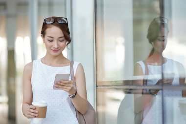 Kahve tutarak ve smartphone kullanarak gülümseyen zarif genç kadın