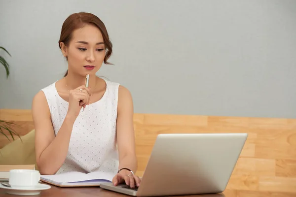 Fundersam Asiatisk Kvinna Som Arbetar Laptop Och Anteckningar Vid Bord — Stockfoto