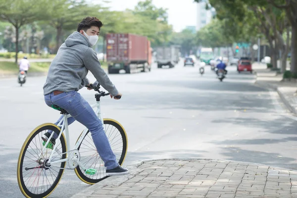 在污染城市骑车时戴口罩的年轻亚裔男子 — 图库照片