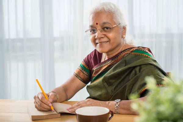 サリのテーブルで日記に書くの陽気な高齢者のインドの女性 — ストック写真