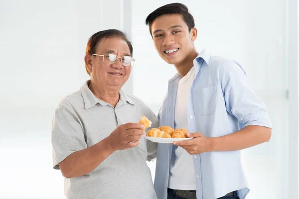 Cheerful Vietnamese Teenager Bringing Plate Croissants Grandfather — Stock Photo, Image