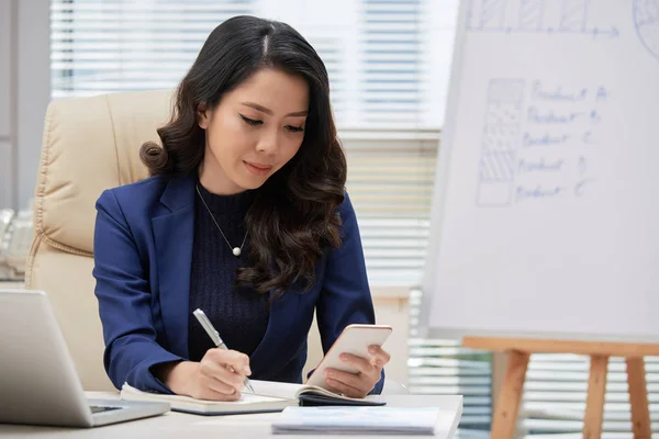Asiatische Geschäftsfrau Sitzt Schreibtisch Und Benutzt Smartphone Während Sie Notizen — Stockfoto