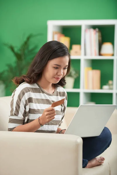 Young Asian woman with laptop making orders from online store, holding credit card