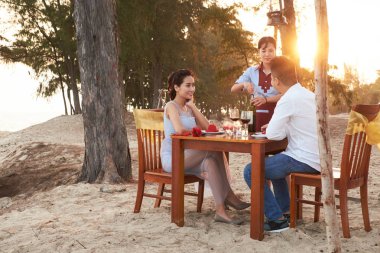 Gün batımında romantik tarih: kırmızı şarap şişesi garsonla plaj Restoran, masada oturan sevgi genç çift