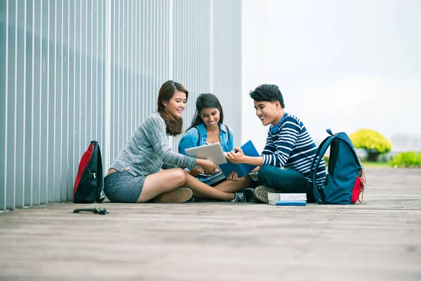 タブレット コンピューターを使用して屋外の地面に座って笑顔の大学生 — ストック写真