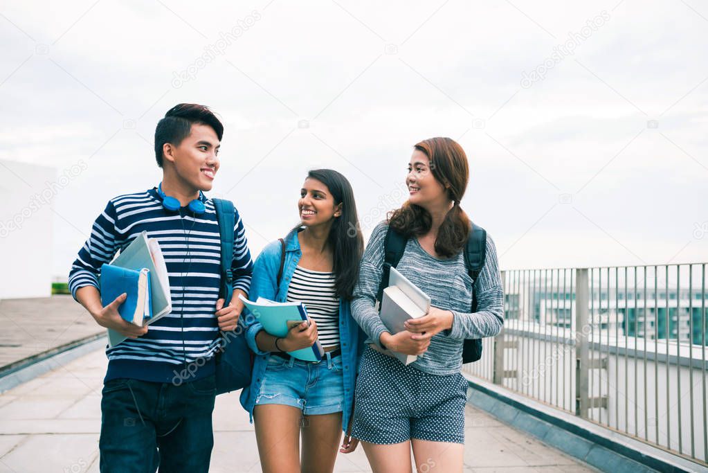 Cheerful classmates with textbooks talking and walking outdoors