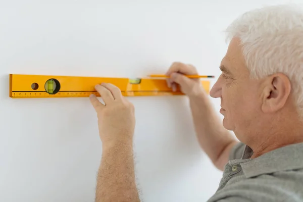 年配の男性が壁建設レベルを測定 — ストック写真
