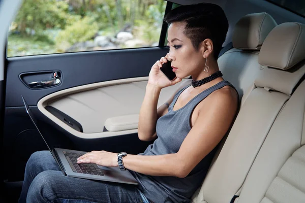 时髦的亚洲妇女坐在她的汽车后座繁忙的工作 — 图库照片
