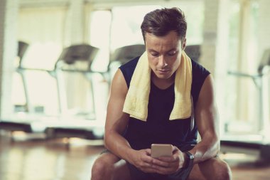 Smartphone vasıl seyir ve modern bir spor salonu bankta oturan yakışıklı genç sporcu