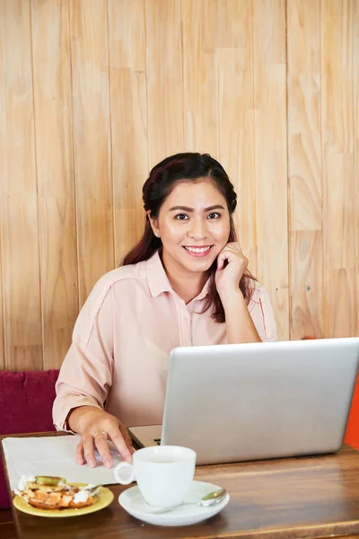 smiling woman working with laptop at cafe table