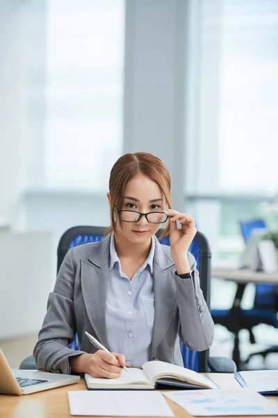 Portrait of serious manager working at office, looking at camera and adjusting glasses