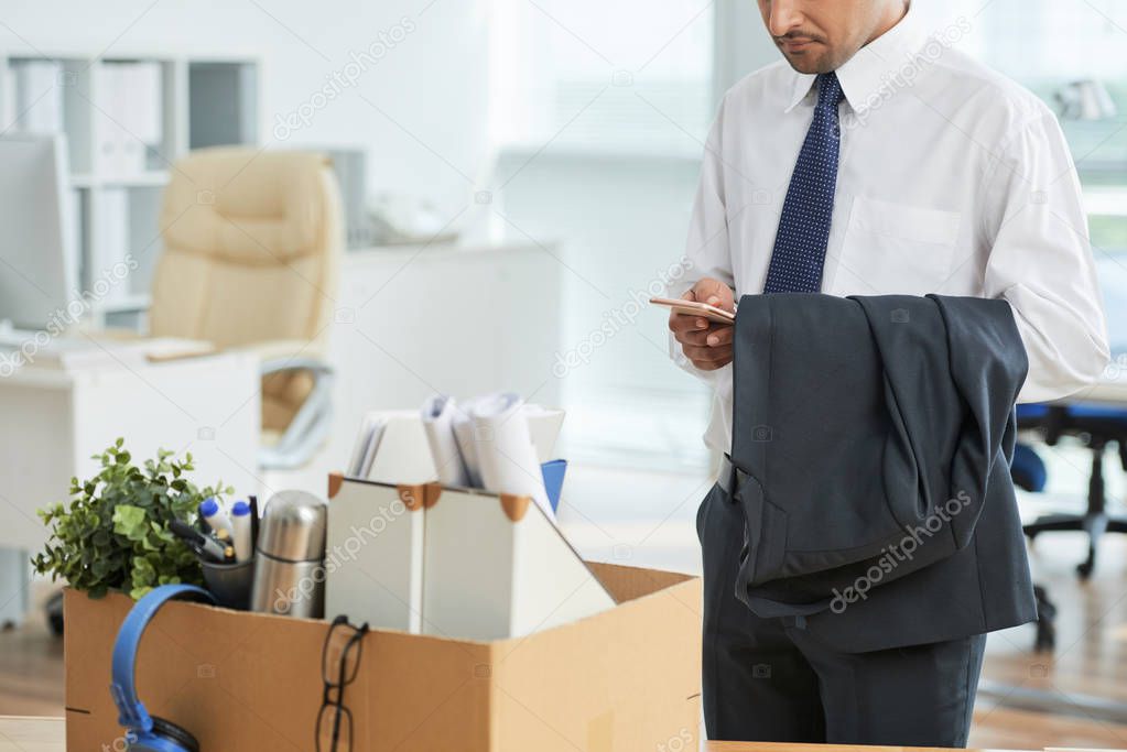 Businessman using mobile phone while packing his stuff into the box