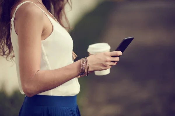 Cropped image of woman with cup of coffee reading messages on phone