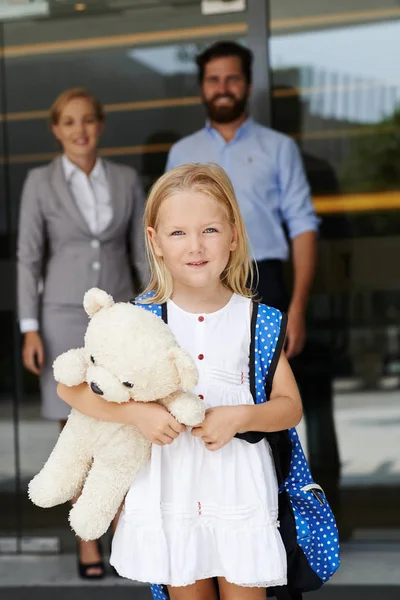 バックパックとテディベアの背景に親に学校に行くと陽気な少女 — ストック写真