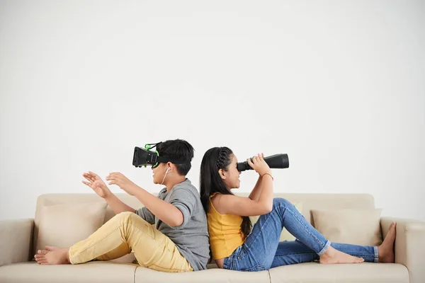 两个亚洲儿童在沙发上在家 男孩穿着 护目镜 女孩看着望远镜 — 图库照片