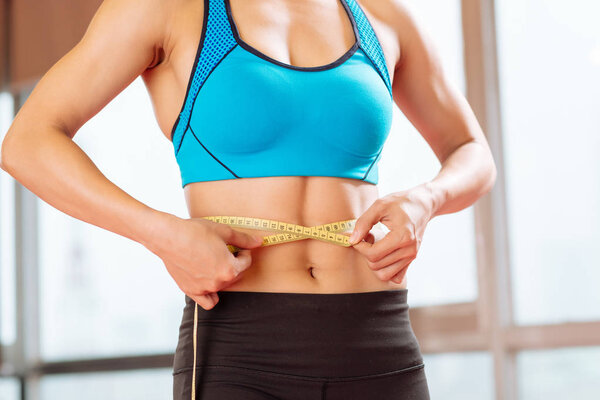 Cropped image of slim woman measuring her waist