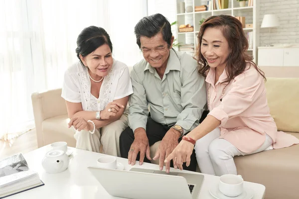 亚洲老人在客厅里用咖啡杯在桌子上浏览笔记本电脑 — 图库照片